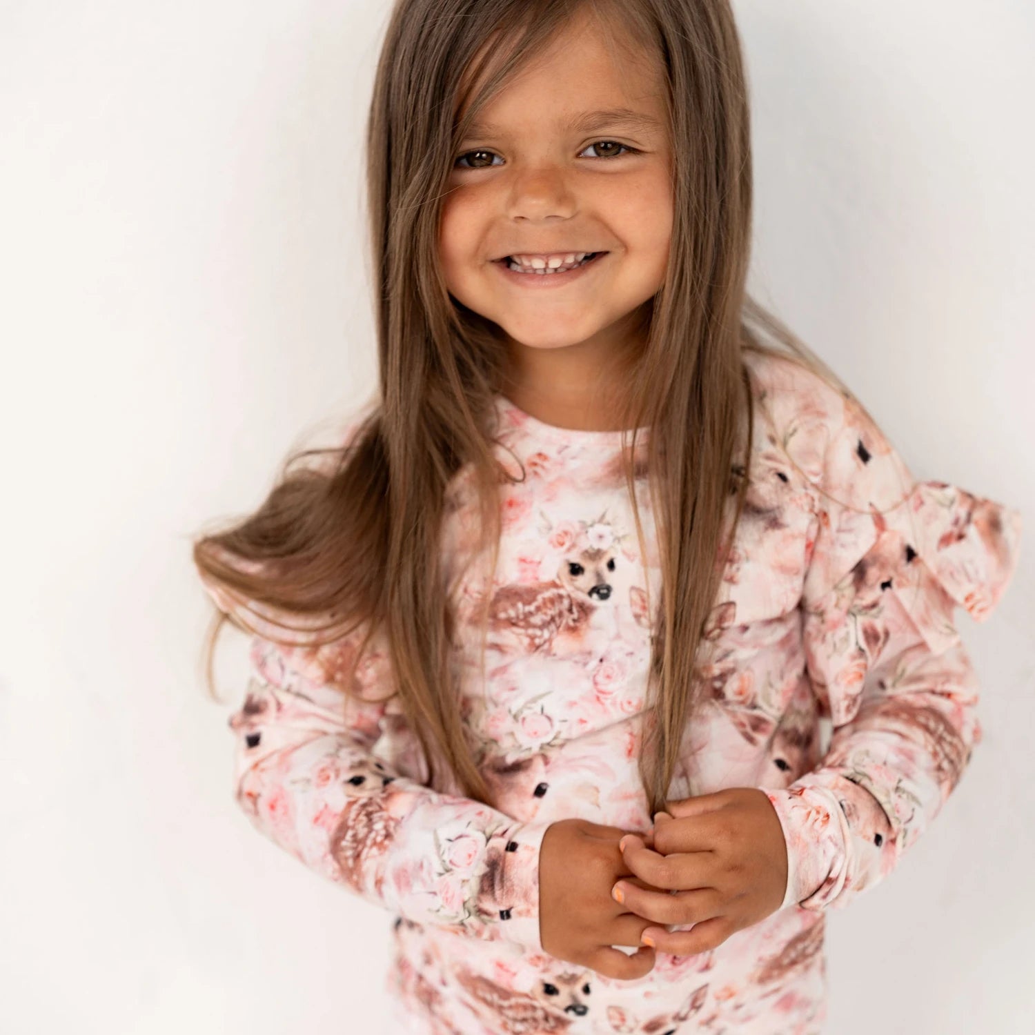 Hymyilevä tyttö Gugguu frillapaidassa ja bambibloom-printissä poseeraa valkoista seinää vasten