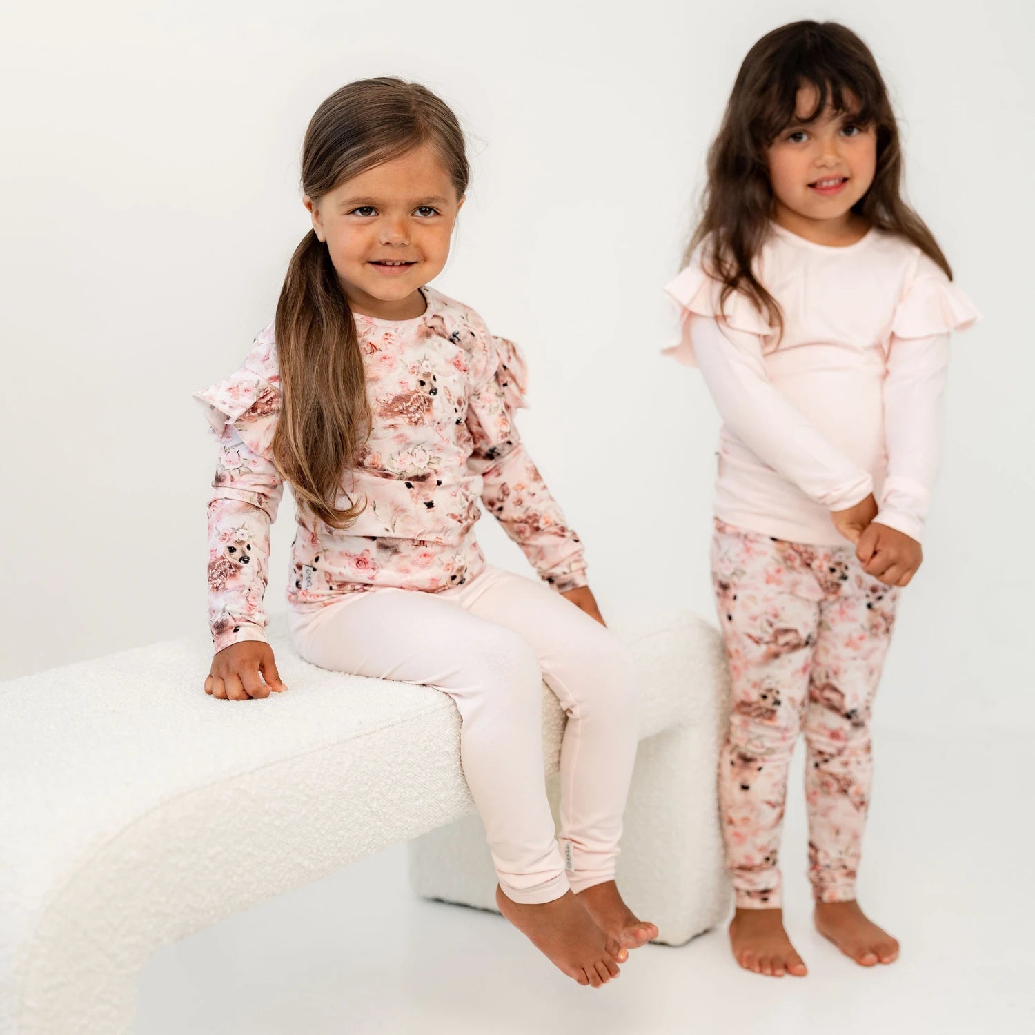 Kaksi lasta istuu vierekkäin. Molemmilla yllään leggingsi ja frilla paidat bambi printillä
