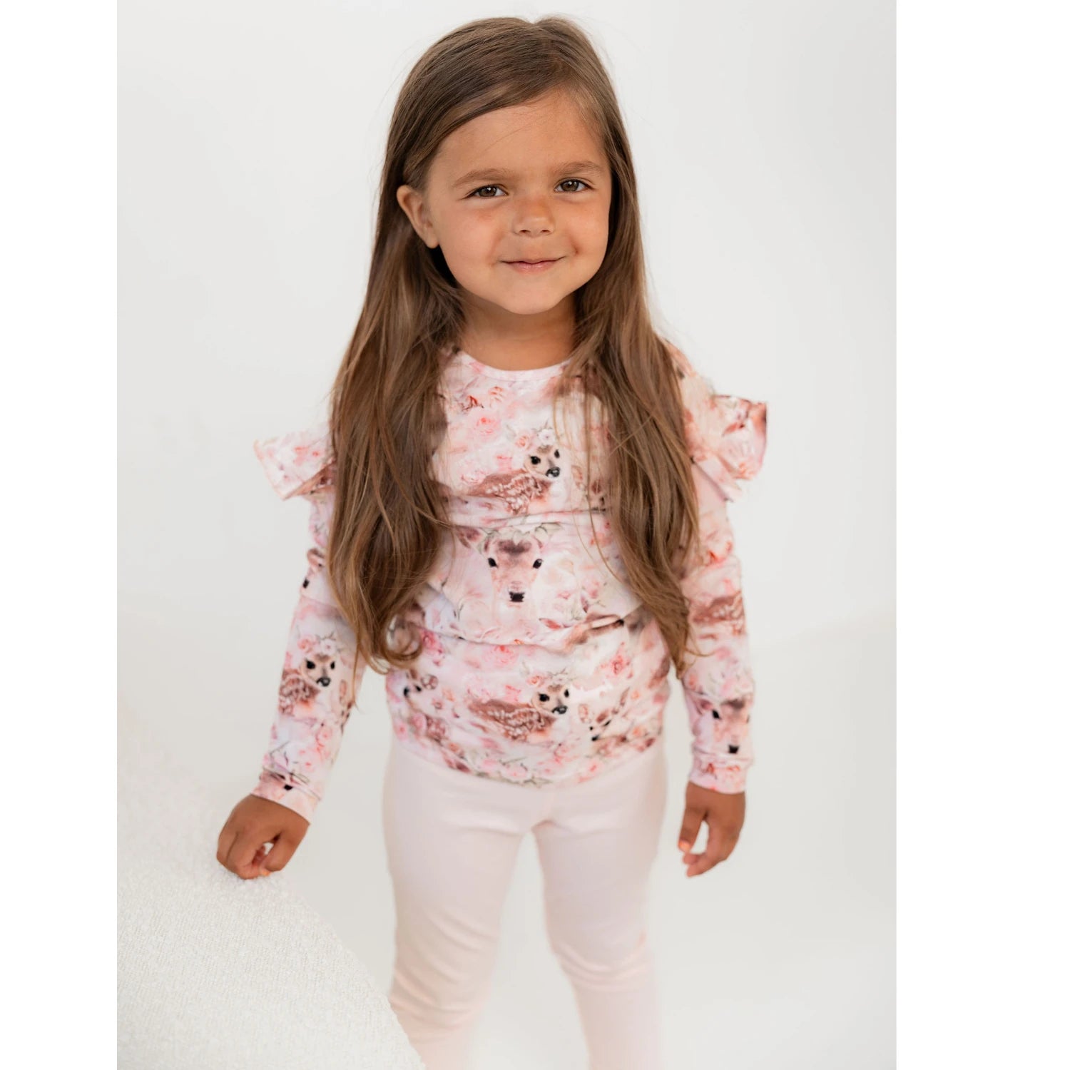 Hymyilevä lapsi pukeutuneena suloiseen bambi paitaan ja vaaleanpunaisiin leggingseihin