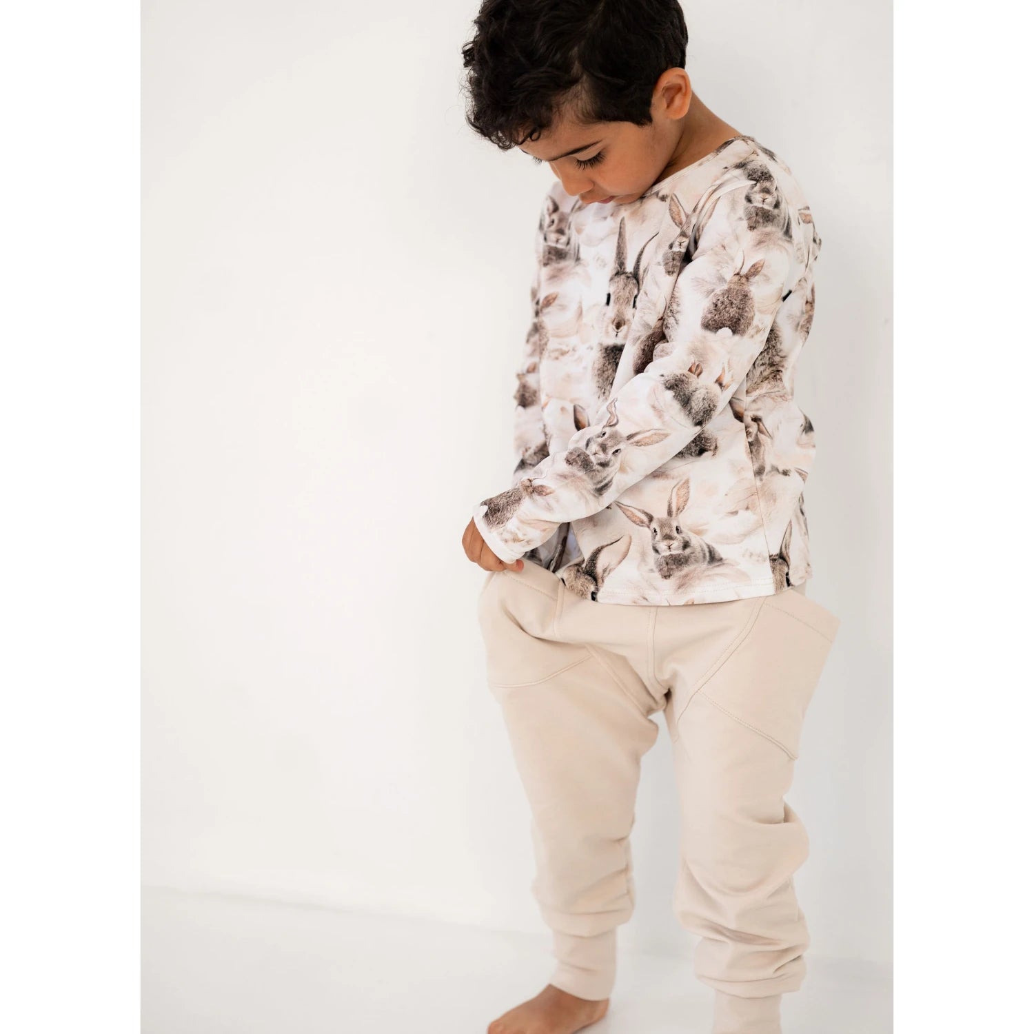 Poika katsoo alaspäin pukeutuneena pupu printtiseen pitkähihaiseen ja beigeihin collegehousuihin.