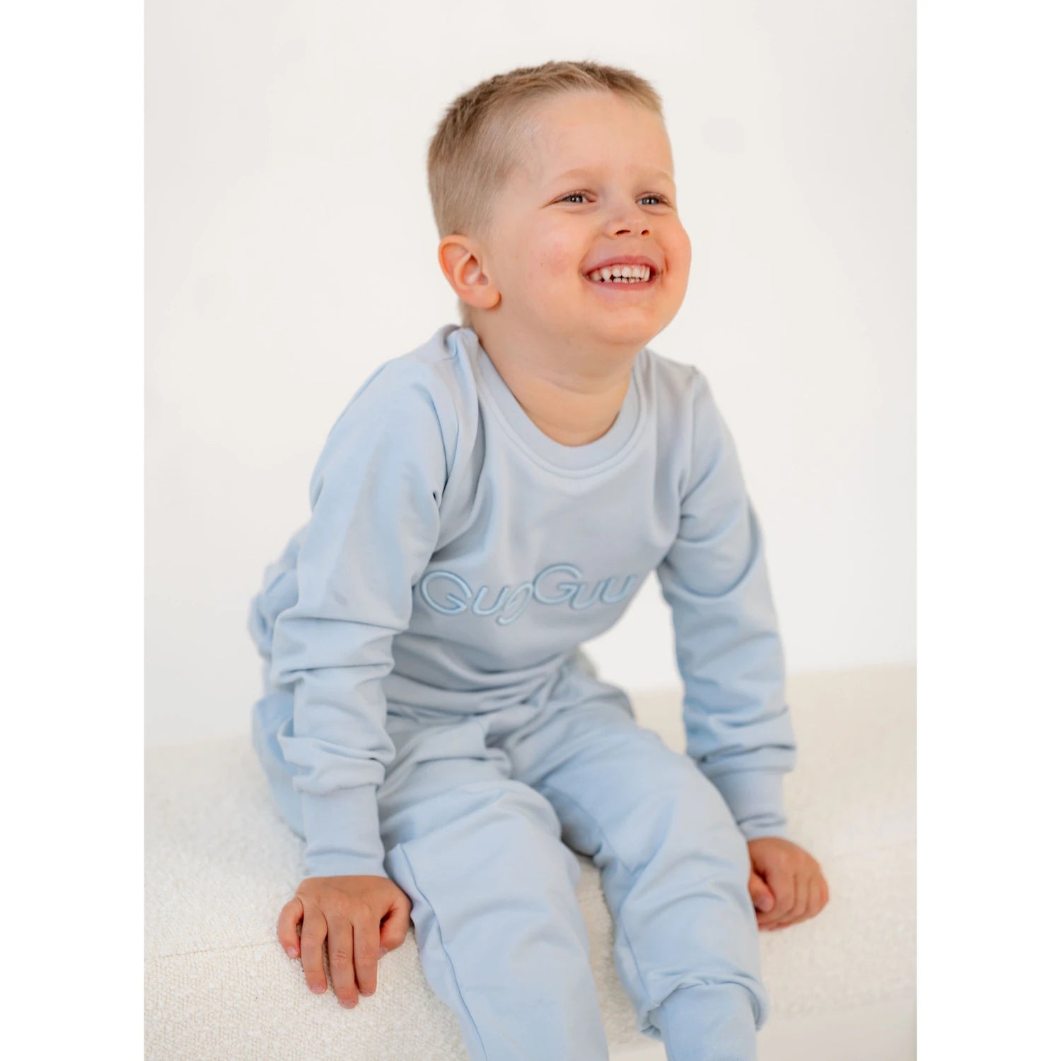 [ALL] Hymyilevä poika vaaleansinisessä college setissä istumassa penkillä