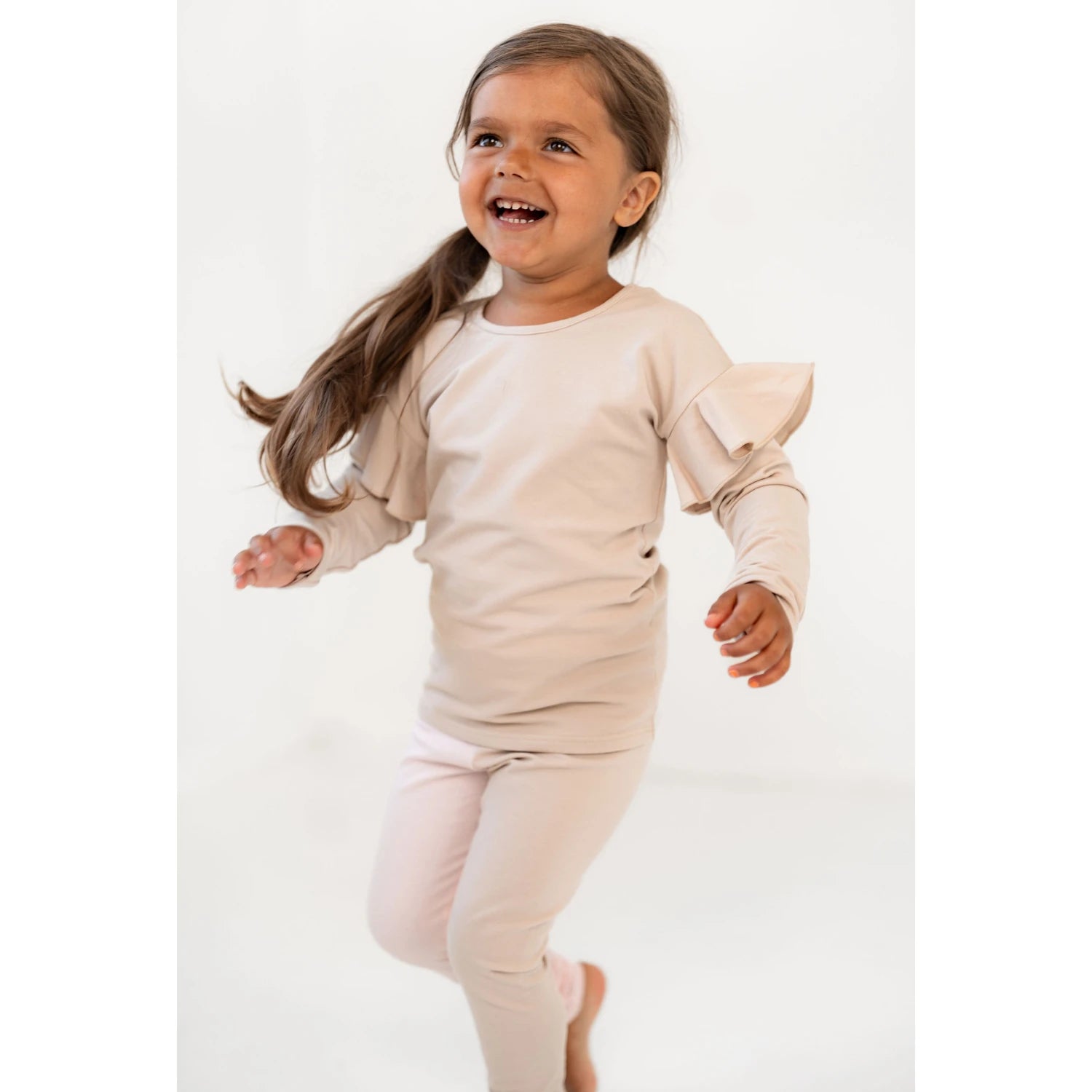 [ALL] Hymyilevä lapsi juoksee vaaleassa frillahihasessa paidassa ja leggingsseissä