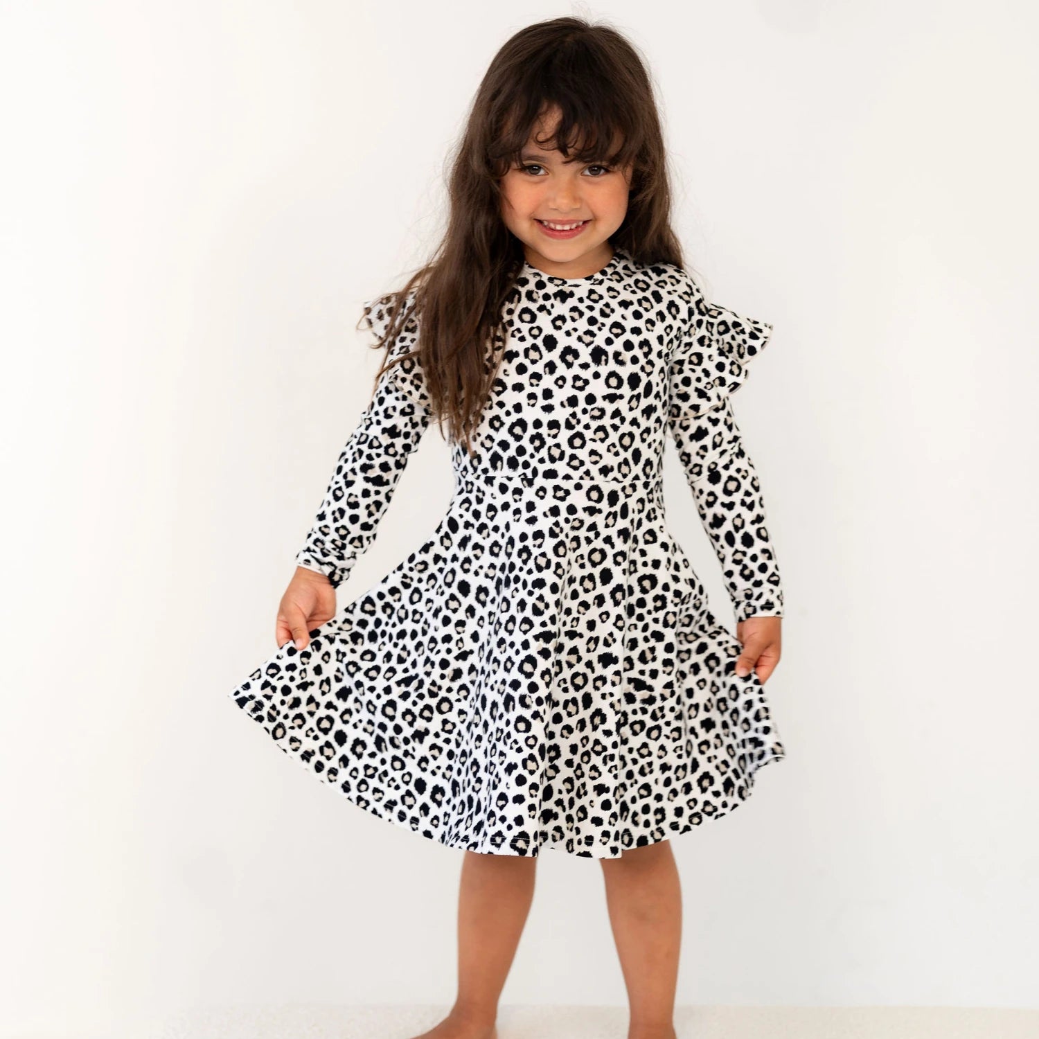 Lapsi iloisena pyörähtelemässä mekossa, jossa on mustavalkoinen beigeleo-kuosi ja A muotoinen helma