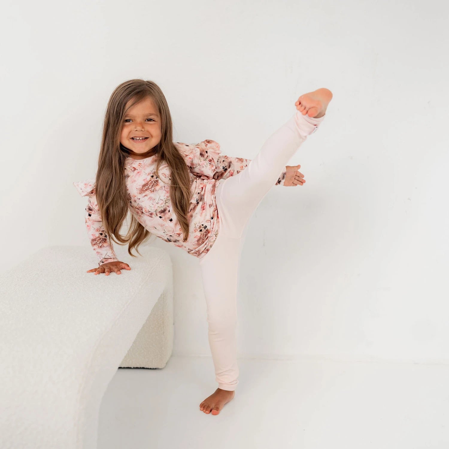 Lapsi leikkisästi nostamassaa jalkaa ylös päällään pinkki bambi paita ja vaaleat leggingsit