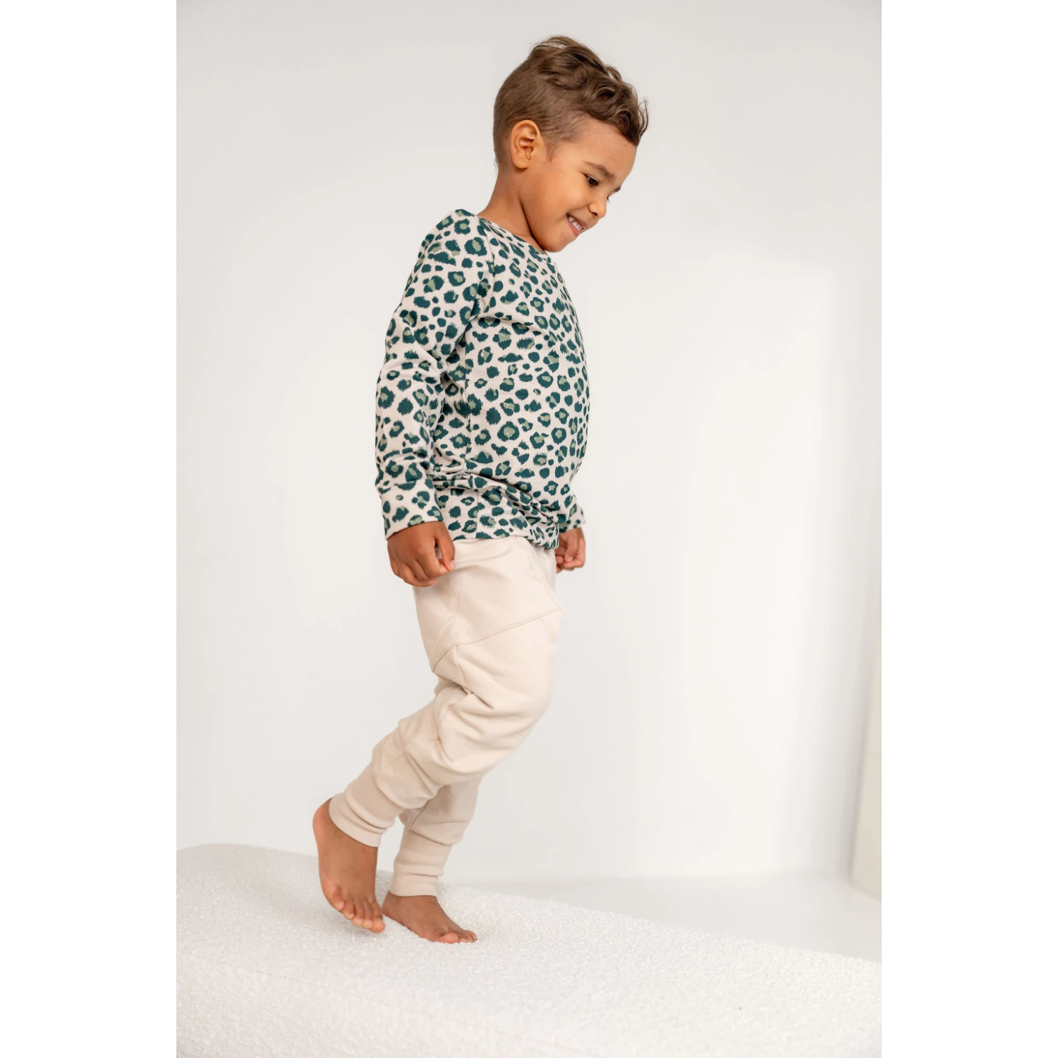 Poika hymyillen kävelemässä. Leopardi kuosillinen collegepaita ja beiget collegehousut päällä.