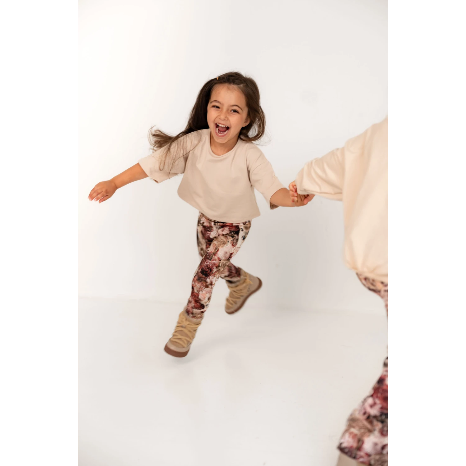 Tyttö leikki iloisena beige t-paita ja tummanpunaiset bambi leggingsit päällään