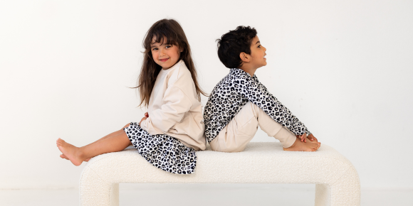 Klassikko malliston julkaisu. Kaksi lasta istuu valkoisella penkillä beigeä ja leopardi printtiä päällä