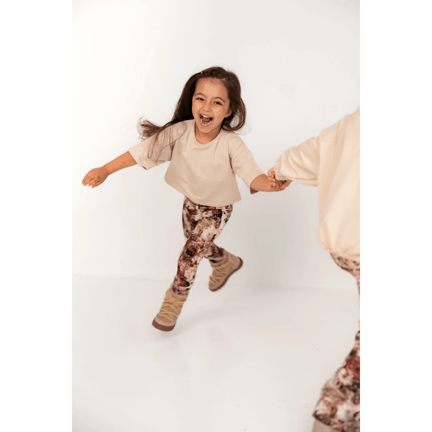 Tyttö leikki iloisena beige t-paita ja tummanpunaiset bambi leggingsit päällään